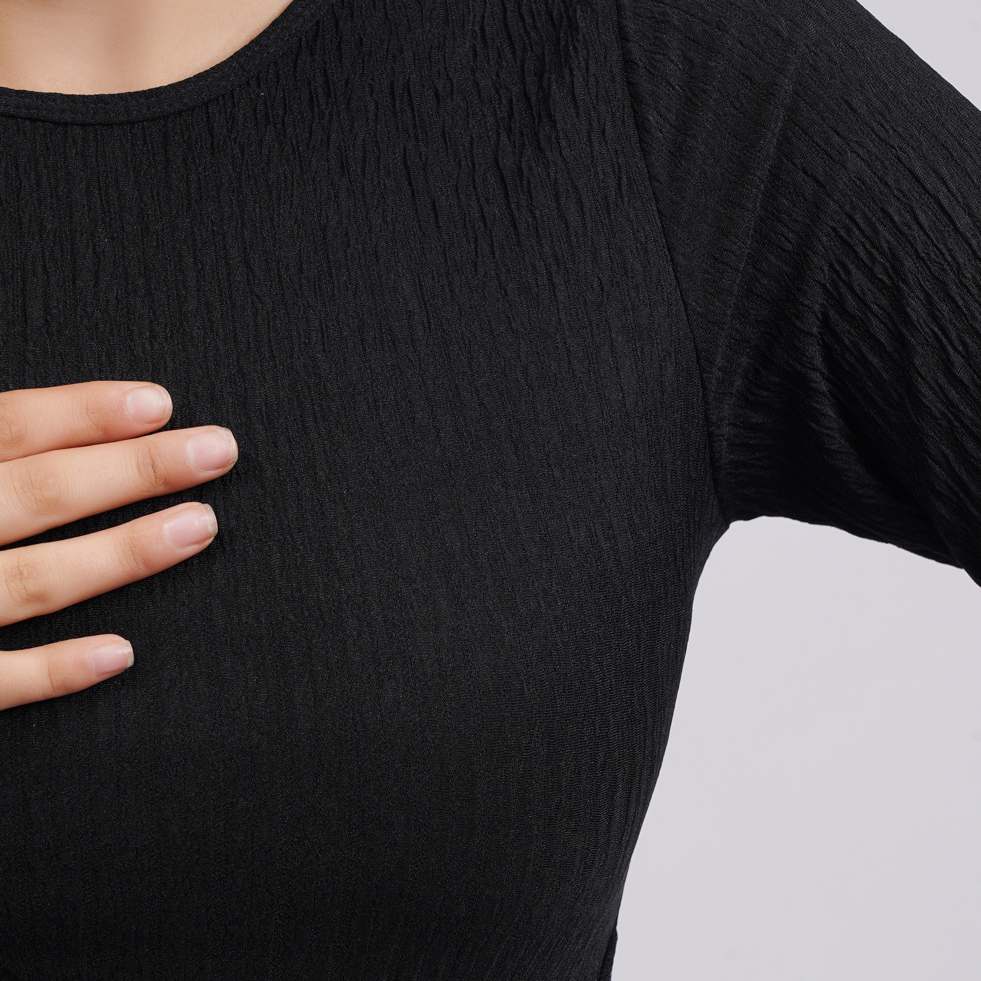 Person wearing a black textured shirt with a neutral background